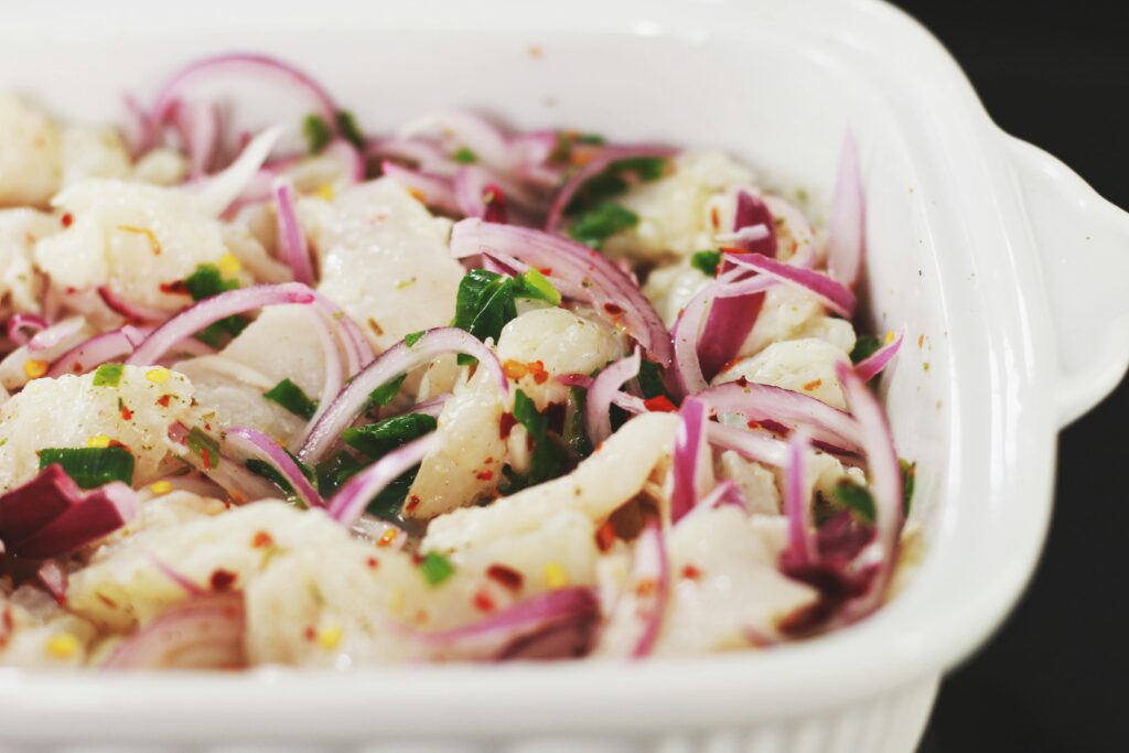 Close-up of a homemade ceviche with red onions and herbs in a white dish, perfect for a refreshing meal.